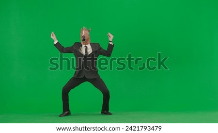 A man in a business suit with a horse head mask on a green studio background. Businessman dancing merrily. Hard office work concept.