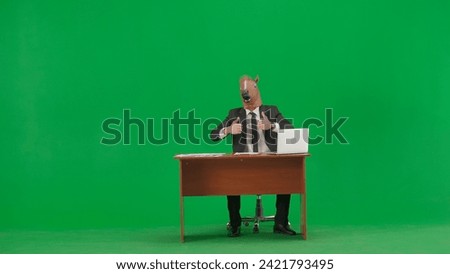 Man in business suit with horse head mask on studio green background. Businessman sitting at desk and showing thumbs up gesture. Hard office work concept.