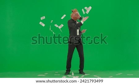A man in a business suit with a horse head mask on a green studio background. Businessman happily scatters banknotes. Hard office work concept. Royalty-Free Stock Photo #2421793499