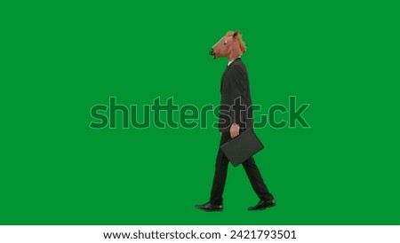 Man in business suit with horse head mask on green studio background. Businessman walking with black suitcase in his hands. Hard office work concept. Side view.