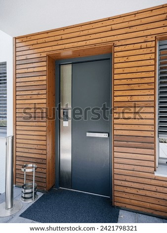 A modern wooden door with multiple secure points, accompanied by an interphone system and a CCTV camera on the left, exemplifying the security features of this property in the real estate market Royalty-Free Stock Photo #2421798321