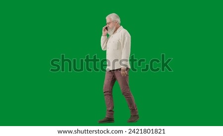Portrait of aged bearded man on chroma key green screen background. Full shot senior man walking and talking on smartphone, side view.