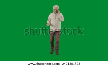 Portrait of aged bearded man on chroma key green screen background. Full shot senior man walking and talking on smartphone, front view.