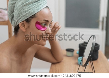 close up woman applies pink under-eye patches, enhancing her skincare with professional cosmetics as she gazes in the mirror. 