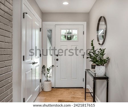 A cozy entryway with brown and brick walls, hardwood flooring, decorations, and a white front door with windows. Royalty-Free Stock Photo #2421817615