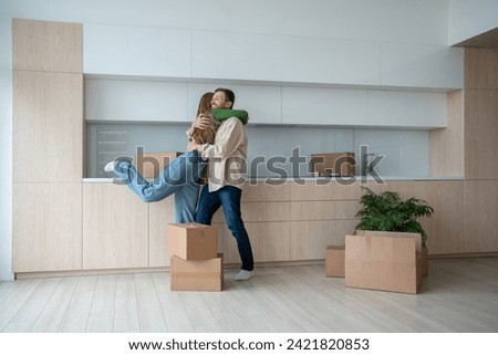 Overjoyed wife and husband hugging on kitchen moving to new flat among cardboard boxes. Relocation, family mortgage, buying apartment, real estate. Happy emotional couple spouses enjoying life changes Royalty-Free Stock Photo #2421820853