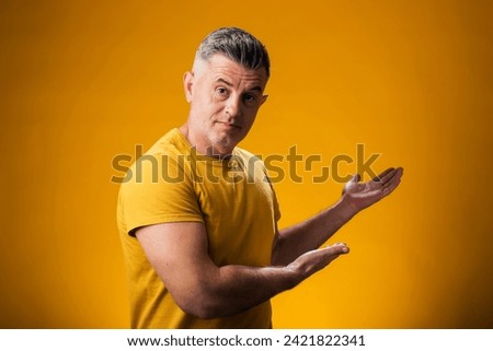Portrait of man smiling cheerful presenting and pointing with palm of hand looking at the camera over yellow background. Advertisement concept
