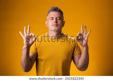 Portrait of man meditating with closed eyes, keeping calm, over yellow background. Relaxation concept