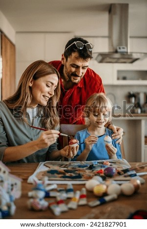 family of three expressing creativity as they paint Easter eggs for the upcoming celebration Royalty-Free Stock Photo #2421827901