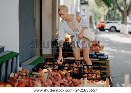 Woman handpicking peaches from a market crate on a bright summer day Royalty-Free Stock Photo #2421835657