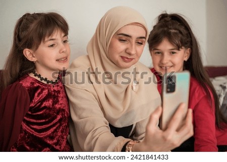Muslim mother and her kids are calling on smartphone. Happy smiling mother and daughters with smartphone having video call at home. High quality photo