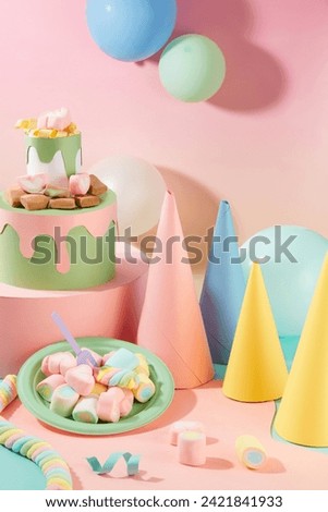 Birthday hats and balloons are displayed next to a three-tier origami birthday cake and a plate of marshmallows. Cute pink background for birthday theme.