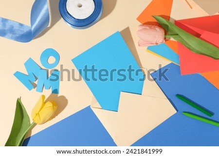 Different items for Women’s Day concept are arranged such as a blank paper inside an envelope, flowers, ribbon roll, crayons, few letters and a stack of colorful paper. Copy space