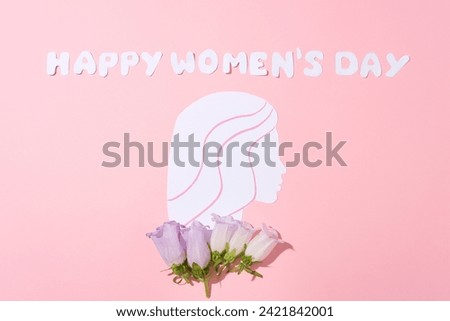 White letters combined form the word Happy Women’s Day over pink background with a paper cut in a woman shaped and some flowers. Elegant card for International Women's Day