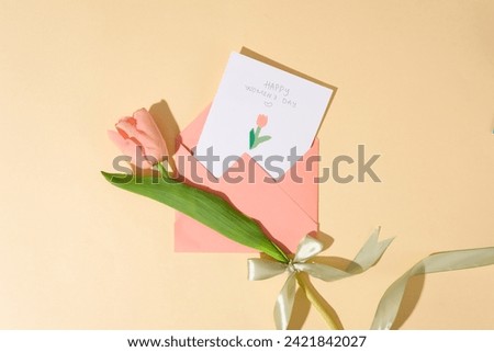 Top view of an envelope in pink color featured a paper with the text “Happy Women's Day” and a paper tulip flower. The earliest reported Women's Day event, called National Women's Day