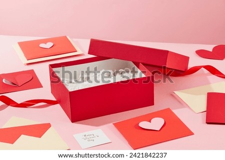 A lot of handmade gift cards are surrounded an opened gift box containing many kraft paper on pink surface. A piece of paper with the text “Happy Women’s Day” featured. Concept for event advertising
