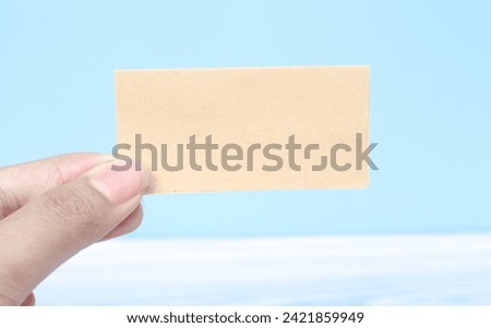 Hand holding a blank piece of paper on a blue background. Blank sheet for writing text on palm. Free space for text and ads