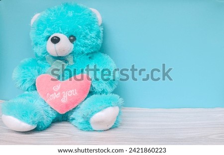 Bright blue bear and pink heart with words I love you on blue background. Bear holding a heart that says I love you