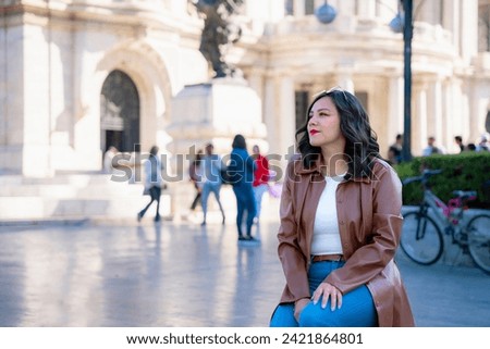 Happy young mexican woman using smartphone and looking at screen of mobile phone while sitting in front of blurred Bellas Fine Arts Palace in Mexico City and wearing fancy clothes