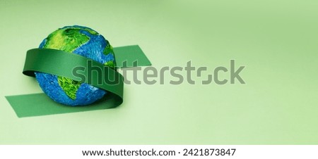 World Earth Day Concept. Green Energy, ESG, Renewable and Sustainable Resources. Environmental Care. Green Ribbon Embracing a Globe. Top View Royalty-Free Stock Photo #2421873847