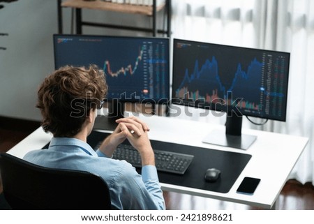 Working young business trader focusing on market stock dynamic graph data in real time two pc screens with back side at modern office. Concept of analyzing dynamic financial exchange rate. Gusher. Royalty-Free Stock Photo #2421898621