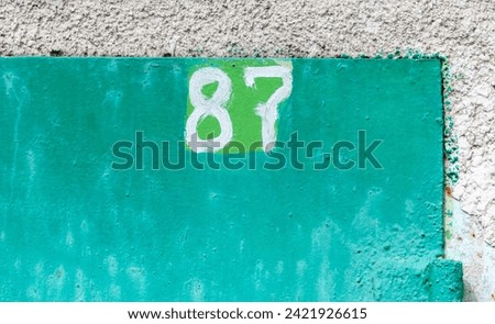 The number 87 on a rusty metal fence.