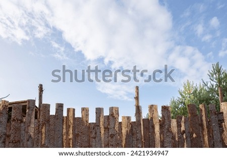 Old wooden fence on a background of blue sky with white clouds. Background and texture. Abstract frame and copy space. Ancient Wooden rustic rural fence and nature landscape