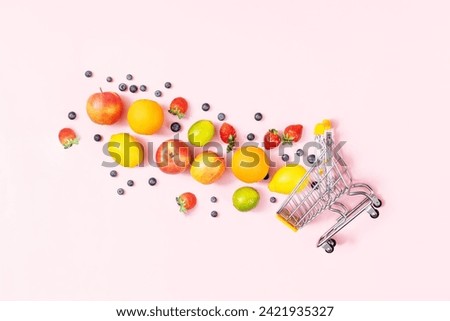 Shopping trolley with fruits on pink background, table top view