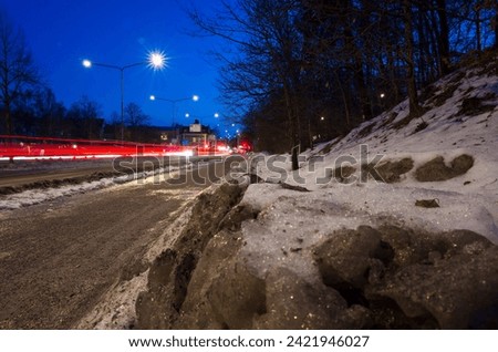 Gray dirty snow next to a path on the side of the road, long exposure photography of traffic at dusk in Västerås, Sweden