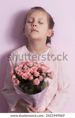 A cute little girl in a pink dress holds a bouquet of pink roses on a pink background
