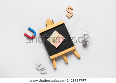 Light bulb with blackboard, symbols of dollar and magnet on grey background. Business idea concept