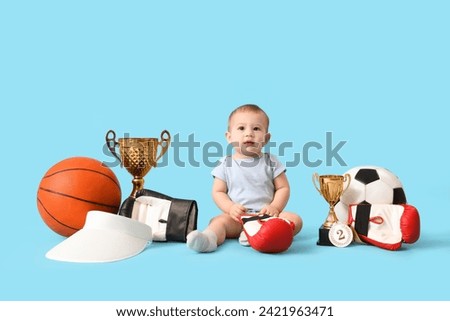 Cute baby athlete with sports equipment on blue background