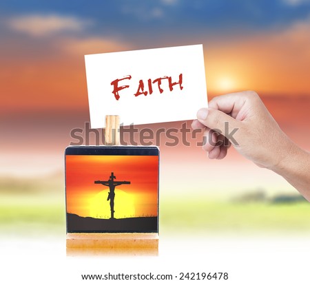 Human hand holding a handwritten FAITH and picture of Jesus with the cross on paper clip.