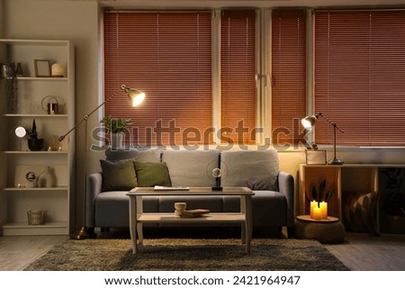 Interior of modern living room with grey sofa, burning candles and glowing lamps at evening Royalty-Free Stock Photo #2421964947