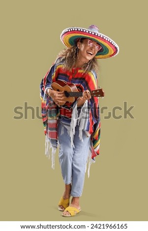 Mature woman in sombrero hat playing guitar on color background. Mexico's Day of the Dead (El Dia de Muertos) celebration Royalty-Free Stock Photo #2421966165