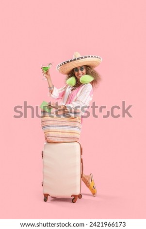 Mature woman in sombrero hat with cocktail and suitcase on pink background. Mexico's Day of the Dead (El Dia de Muertos) celebration Royalty-Free Stock Photo #2421966173