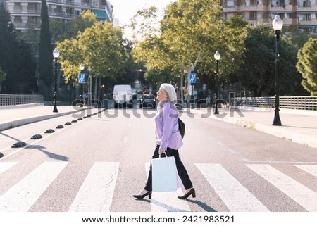 senior woman crossing a street with shopping bags Royalty-Free Stock Photo #2421983521