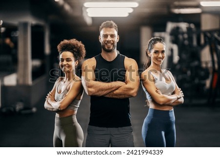 Portrait of a personal trainer with sportswomen posing in a gym with arms crossed and smiling at the camera. Royalty-Free Stock Photo #2421994339