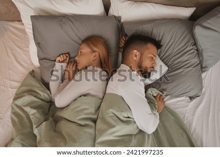 Displeased couple lying back to back on a bed and ignoring each other Royalty-Free Stock Photo #2421997235