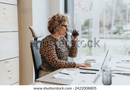 Taking a break from a demanding work session, a senior female worker revitalizes herself with a sip of juice. Royalty-Free Stock Photo #2422008805