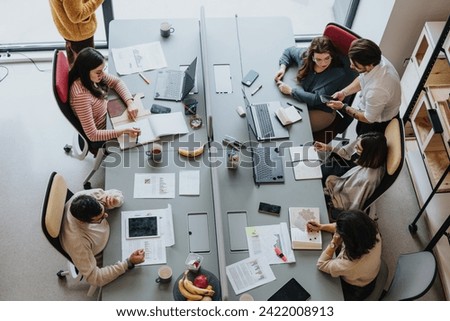 Coworkers collaborate and work together in a modern office. They discuss tasks, use laptops, and smile. This successful team represents a multicultural and multi-generational workforce. Royalty-Free Stock Photo #2422008913