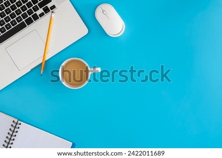 Laptop with notebook and cup of coffee on blue background.