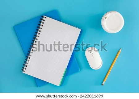 Notebooks, computer mouse and cup of coffee on a blue background, top view.