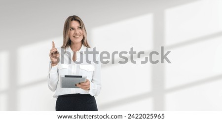 Happy young European woman holding tablet computer and standing with finger pointing up over white copy space background. Concept of good idea and brainstorming