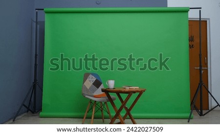 Wide picture of a set-up in front of green backdrop with tripod stand