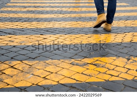 A person crosses yellow pedestrian crossings. Only the pedestrian's shoes are visible.