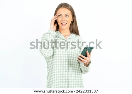 Pleasant looking happy Young beautiful woman wearing green plaid pyjama has nice telephone conversation and looks aside, has nice mood and smiles positively while talks via cell phone Royalty-Free Stock Photo #2422031537