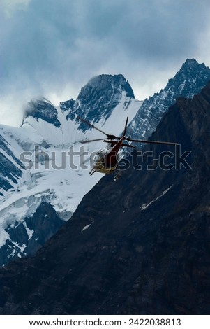 An image of a Red Helicopter travelling through the snowy mountains of Kashmir at an high altitude going through the gaps of the mountains.