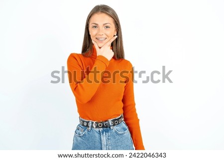 Young beautiful woman looking confident at the camera smiling with crossed arms and hand raised on chin. Thinking positive. Royalty-Free Stock Photo #2422046343