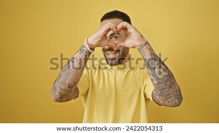 Tattooed man making heart sign with hands on yellow background